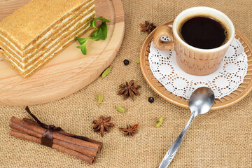 A piece of honey cake on a wooden cutting board, next to a cup of black coffee on a saucer.