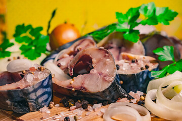 Fresh mackerel fish cut into pieces, with herbs, onions, spices and salt on a wooden board.