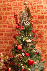 Arbol de navidad con adornos y una angel dorado con fondo de letras navideñas