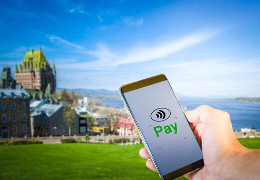 Man Paying Using Smartphone, Cashless Payment Technology Concept With Quebec On The Bakcground. Canada Is One Of The World Leaders In Cashless Payments