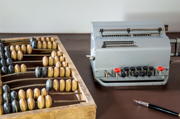 Old wooden abacus, mechanical calculator and fountain pen on a vintage desk.