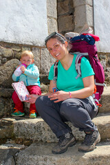 Senderismo. Descanso después de la caminata. Mamá y niño pequeño sentados en un escalón de piedra bebiendo agua con la mochila al hombro. Camino de Santiago