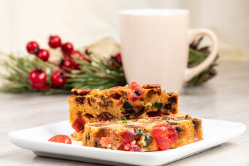 slices of traditional Christmas fruit cake cut with a coffee cup and a pine branch in the background
