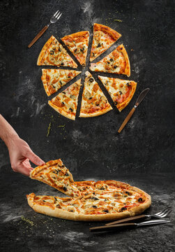 Home made original italian pizza with human hand holding pizza slice. Top view separated pizza slices on black grunge background