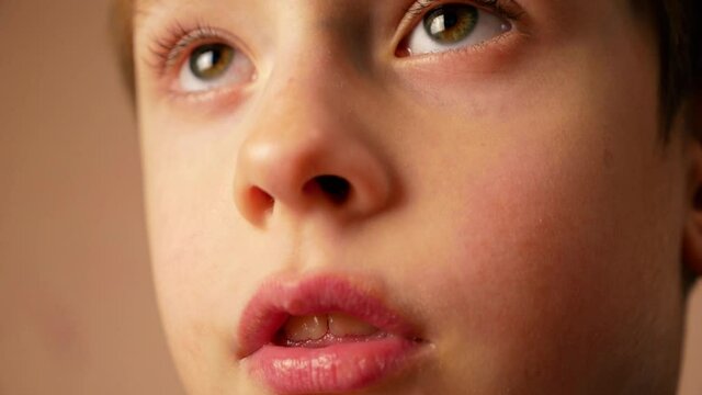 Close-up face of a Caucasian boy 6-7 years old from surprise opening his mouth. The child watches TV attentively and with admiration. Emotional kid. Selective focus, shallow depth of field