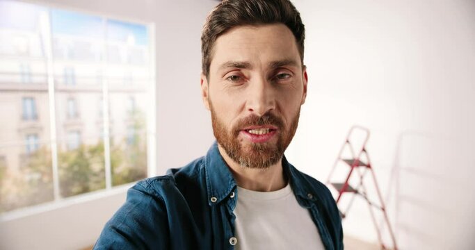 POV of Caucasian happy handsome young bearded man in apartment repairing room videochatting online on webcam with client. Handyman talking on video call. Redesigning and renovating house concept