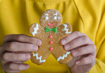 Hands hold a gingerbread man, on a yellow background.