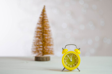 Yellow alarm clock and golden Christmas tree on the table.