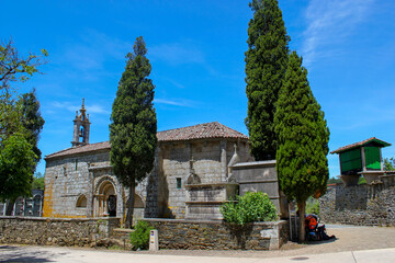 Fototapeta na wymiar Paisaje del camino de Santiago. Iglesia Románica con cipreses y las mochilas de los peregrinos en un ángulo