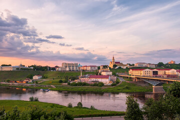 Fototapeta na wymiar Belarus.Sights and views of the city of Grodno. On the riverbank Neman there are the buildings of the theater and the church at illuminated by the rays of the setting sun.