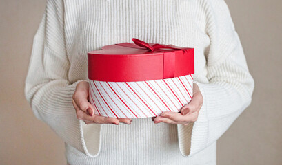 A red gift box is held by women's hands .