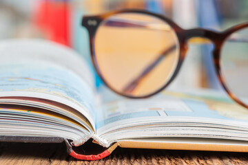 Open book and defocused eyeglasses and bookshelve in the background
