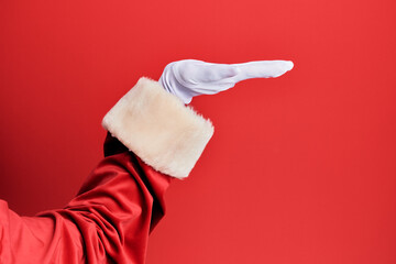 Hand of a man wearing santa claus costume and gloves over red background with flat palm presenting product, offer and giving gesture, blank copy space