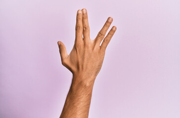 Arm and hand of caucasian young man over pink isolated background greeting doing vulcan salute, showing back of the hand and fingers, freak culture