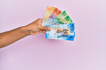 Hispanic hand holding swiss franc banknotes over isolated pink background.