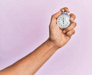 Hand of young hispanic man using stopwatch over isolated pink background.