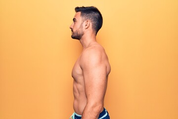 Young handsome man with beard wearing sleeveless t-shirt standing over yellow background looking to...