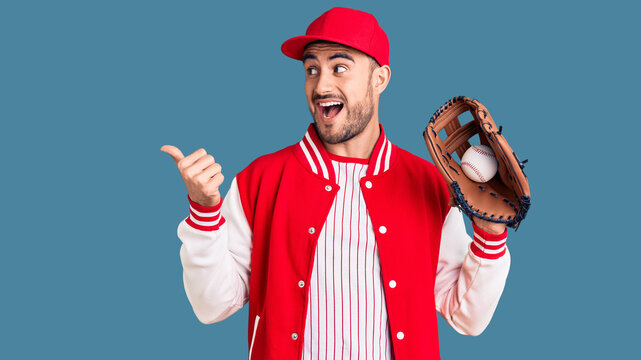 Young handsome man holding baseball gloves pointing thumb up to the side smiling happy with open mouth