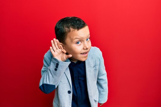 Little Kid Boy Wearing Elegant Business Jacket Smiling With Hand Over Ear Listening And Hearing To Rumor Or Gossip. Deafness Concept.