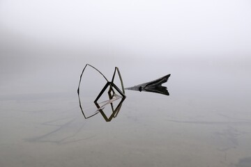 Moody misty landscape of lake with amazing effect of reflection of branches immersed in calm surface of water. Otomin Lake, Kashubia, Poland