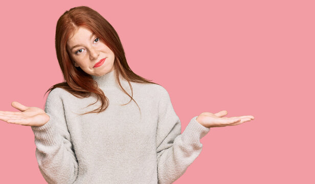 Young read head woman wearing casual winter sweater clueless and confused expression with arms and hands raised. doubt concept.