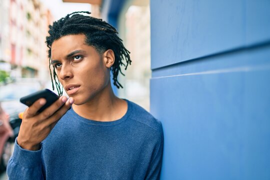 Young african american man with unhappy expression sending audio message using smartphone at street of city.