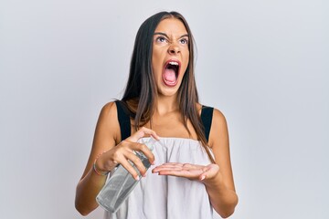 Young hispanic woman using hand sanitizer gel angry and mad screaming frustrated and furious, shouting with anger looking up.