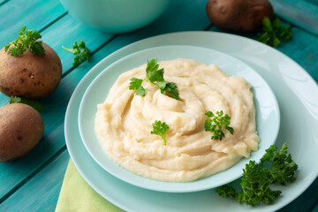 Delicious mashed potatoes with parsley in a turquoise bowl with vegetables.
