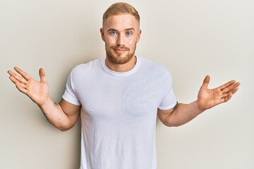 Young caucasian man wearing casual white tshirt clueless and confused with open arms, no idea and doubtful face.