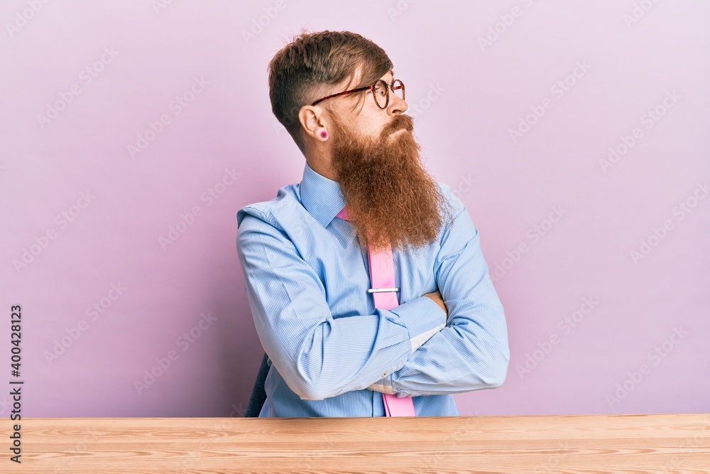 Sticker Young irish redhead man wearing business shirt and tie sitting on the table looking to the side with arms crossed convinced and confident