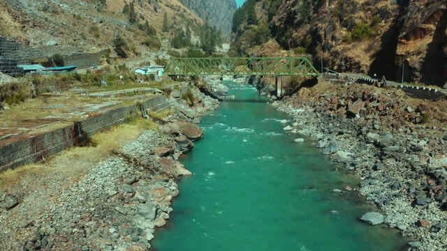 Beautiful Bhagirathi River flowing through small rocks under small green bridge and surrounded by huge mountain region in Uttarkashi,Uttarakhand,India. Aerial view shot on Mavic 2 Pro
