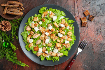 top view caesar salad on oval plate fork bowl with dried crust on dark red background