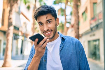 Young latin man smiling happy sending voice message using smartphone at the city.