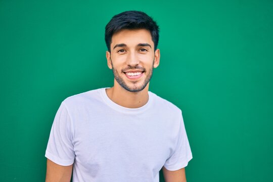 Young latin man smiling happy leaning on the wall at the city.
