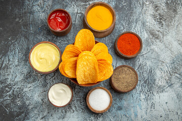 Above view of crispy chips on wooden cutting board and different spices on gray table