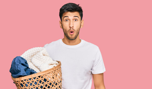 Young handsome man holding laundry basket scared and amazed with open mouth for surprise, disbelief face