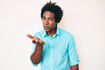 Handsome african american man with afro hair wearing casual clothes looking at the camera blowing a kiss with hand on air being lovely and sexy. love expression.