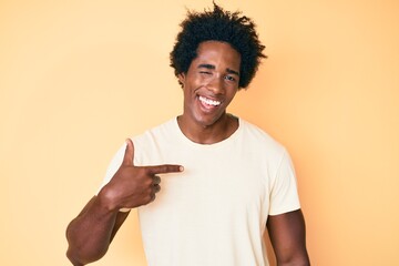 Handsome african american man with afro hair pointing with fingers to himself winking looking at the camera with sexy expression, cheerful and happy face.