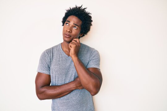 Handsome african american man with afro hair wearing casual clothes thinking concentrated about doubt with finger on chin and looking up wondering