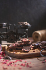 Raw vegan handmade dark Chocolate with dried fruits and berries, wooden rustic table, dark background.  Homemade healthy dessert. Copy space.