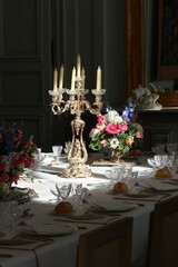 Chandelier en argent posé sur une table dressée pour un repas de fête, avec un bouquet de fleurs