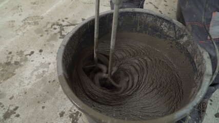 The drill nozzle is inserted into wet cement. Wet mortar mixture for finishing work in construction. Traces of tool rotation. Repair in the household. Close-up, selective focus. 