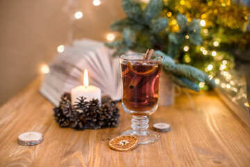 Mulled wine with cinnamon sticks and orange on a wooden table. Burning candle and Christmas tree lights