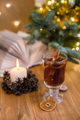 Mulled wine with cinnamon sticks and orange on a wooden table. Burning candle and Christmas tree lights