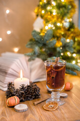 Fototapeta na wymiar Mulled wine with cinnamon sticks and orange on a wooden table. Burning candle and Christmas tree lights