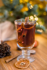 Mulled wine with cinnamon sticks and orange on a wooden table. Burning candle and Christmas tree lights