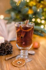 Mulled wine with cinnamon sticks and orange on a wooden table. Burning candle and Christmas tree lights