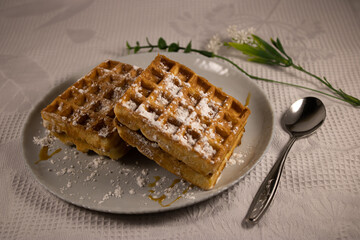 A lovely breakfast: Viennese Belgian waffles decorated with powdered sugar and green twigs on a checkered napkin. Next to it is a teaspoon.
