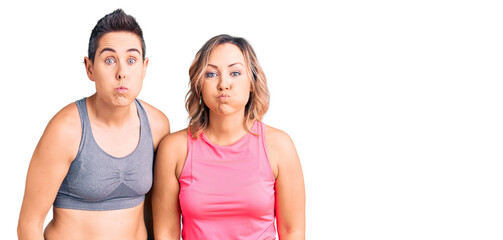 Couple of women wearing sportswear puffing cheeks with funny face. mouth inflated with air, crazy expression.