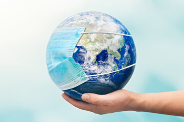 Hand holding Earth globe with face mask